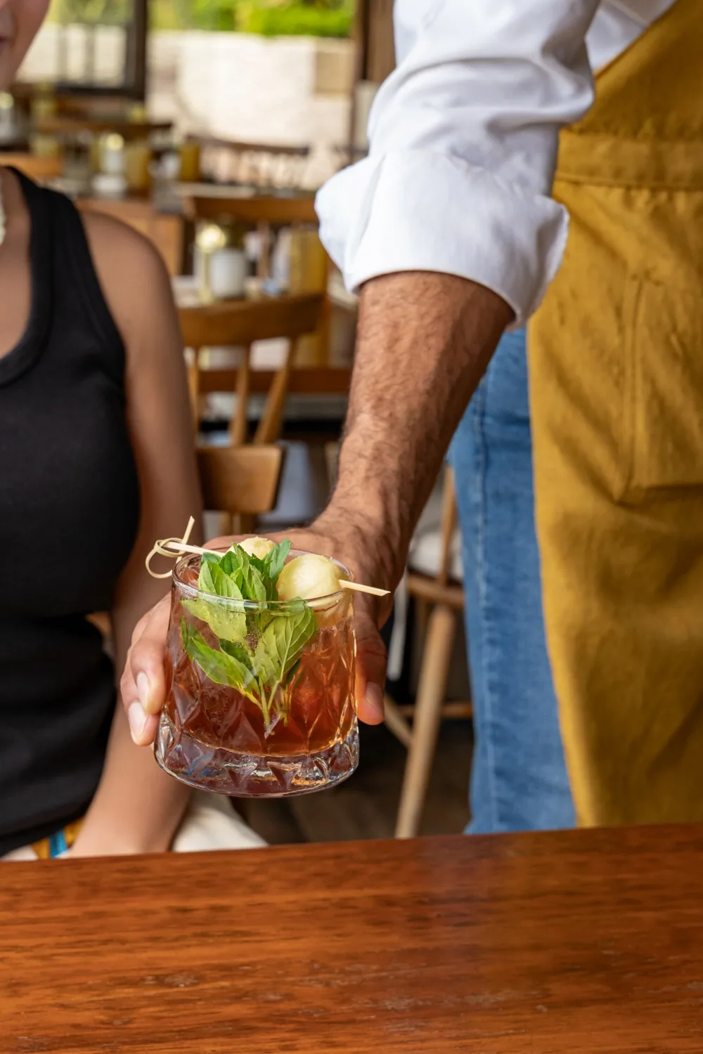 A waiter serving a cocktail with basil and melon at the table