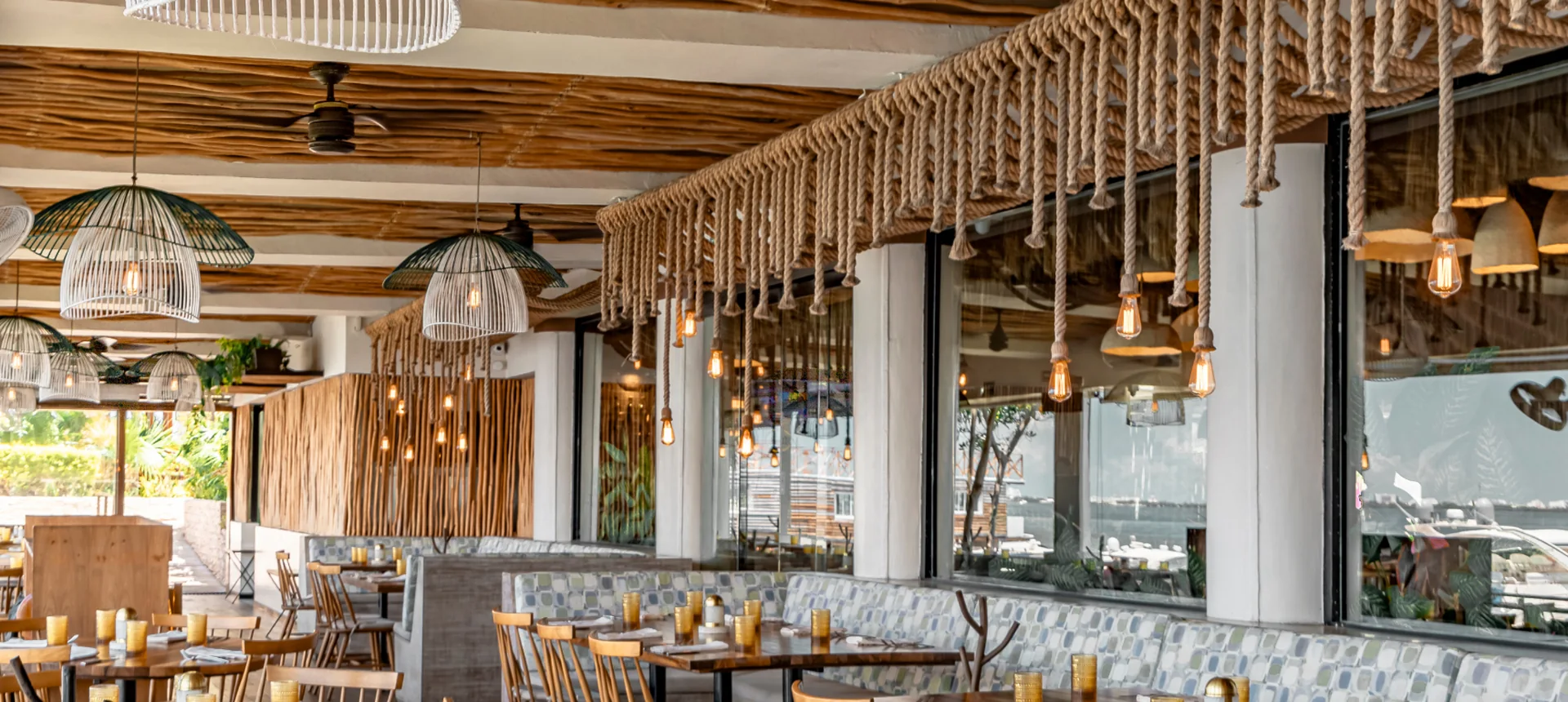 The dining room at Fred’s Cancun: wooden ceiling, hanging ropes and tables laid by the windows