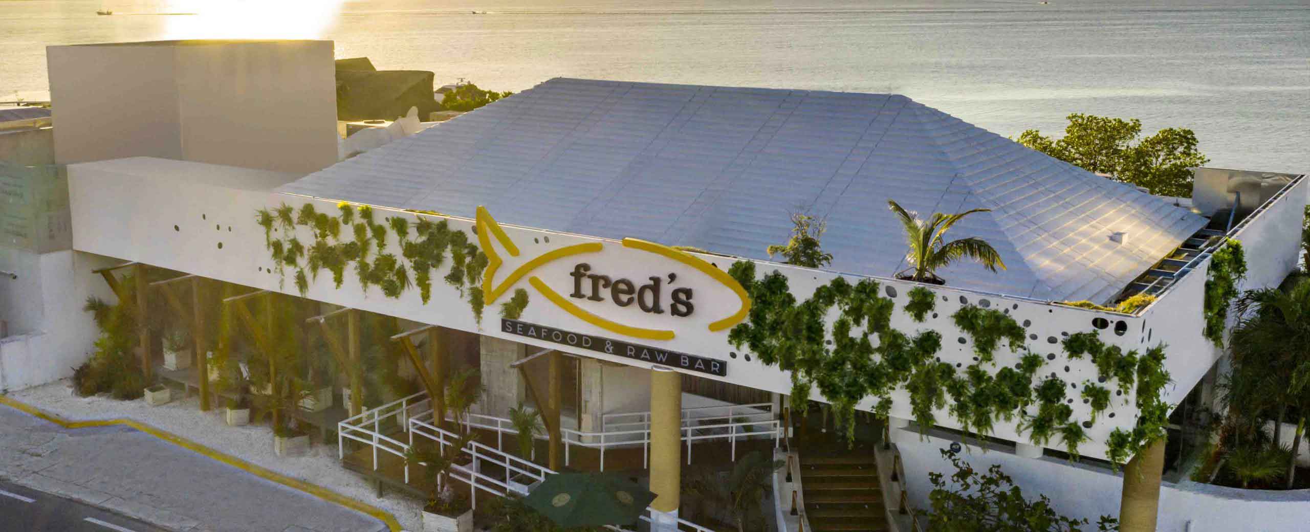 Vista aérea del restaurante Fred's donde se aprecia el frente del lugar y detrás la laguna y el atardecer